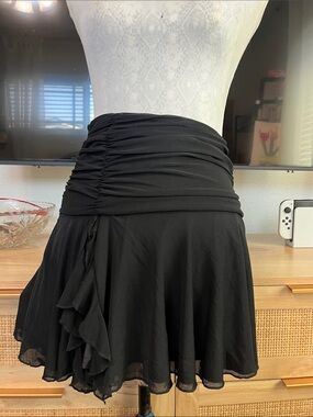 black mini skirt with a heavily ruched waistline and a playful ruffled side hem
